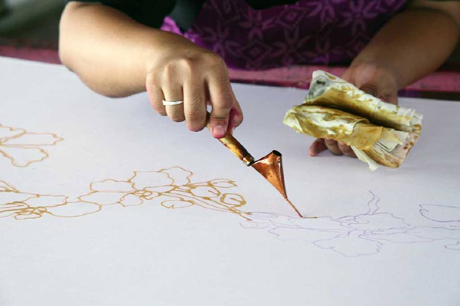 An artist carefully traces the floral motif on a traditional batik fabric using melted wax